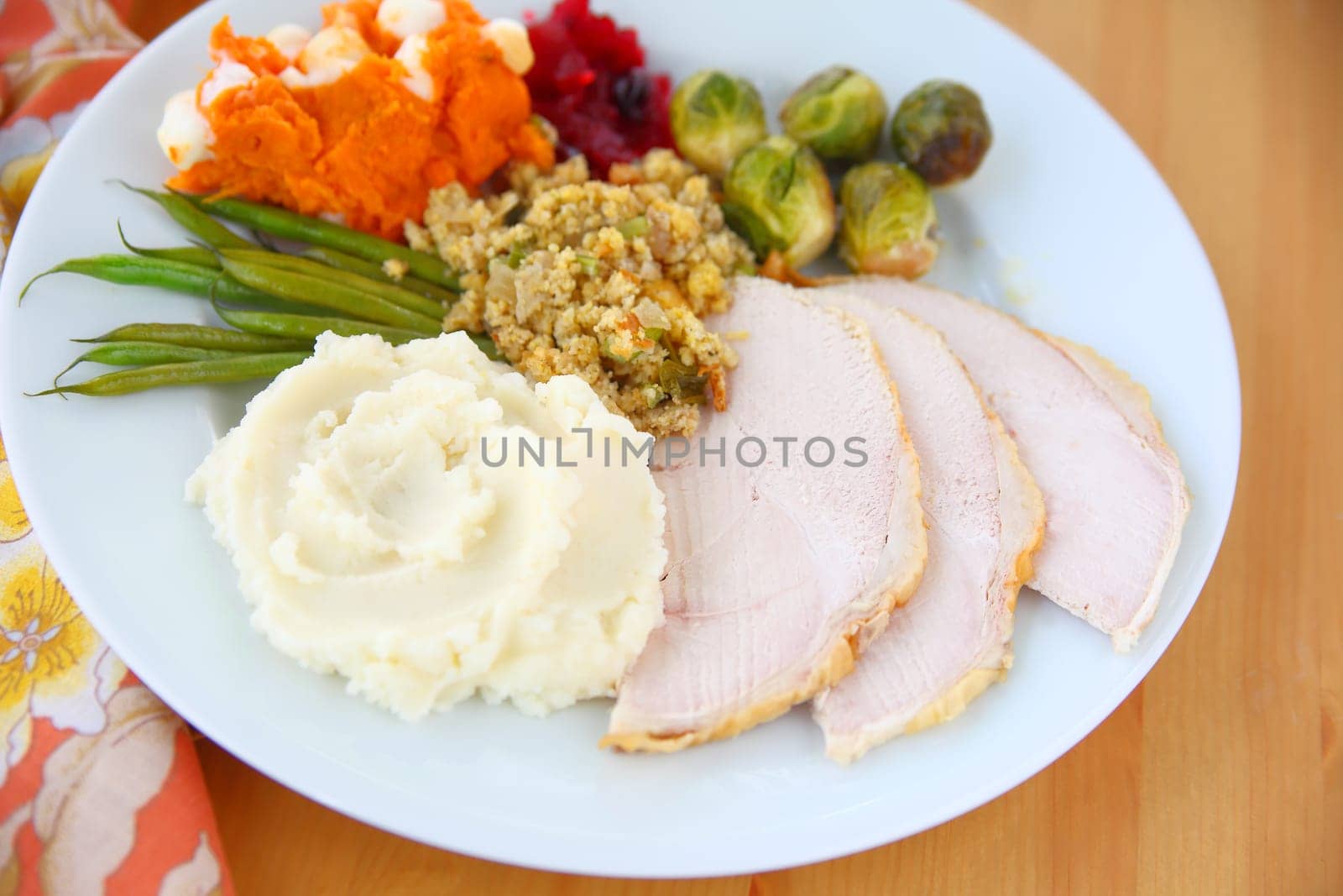 Plate of roast turkey slices, mashed potatoes, stuffing, brussels sprouts, mashed sweet potatoes and green beans with cranberry sauce