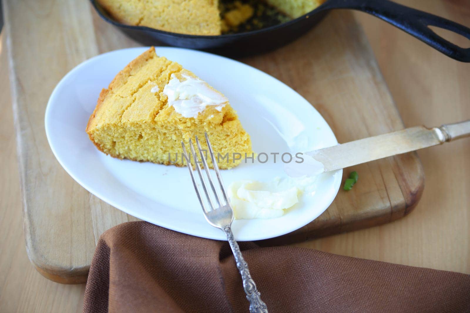 Cornbread wedge with butter with cast iron skillet in background