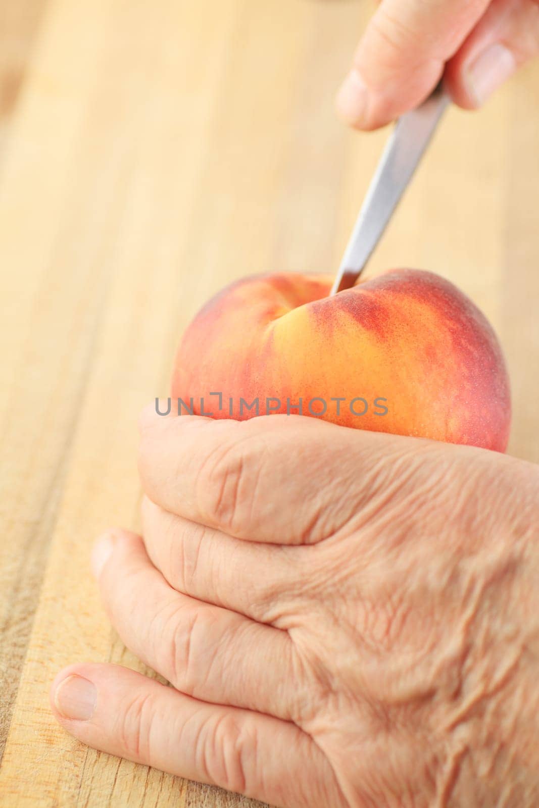 A man cuts into a peach with a paring knife.