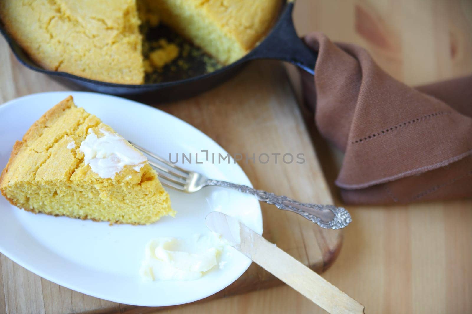 Portion of cornbread with butter with the rest in a cast iron skillet behind