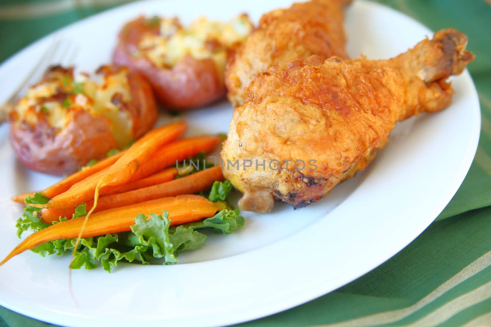 Fried chicken, roasted carrots and crushed potatoes on a white plate with napkin
