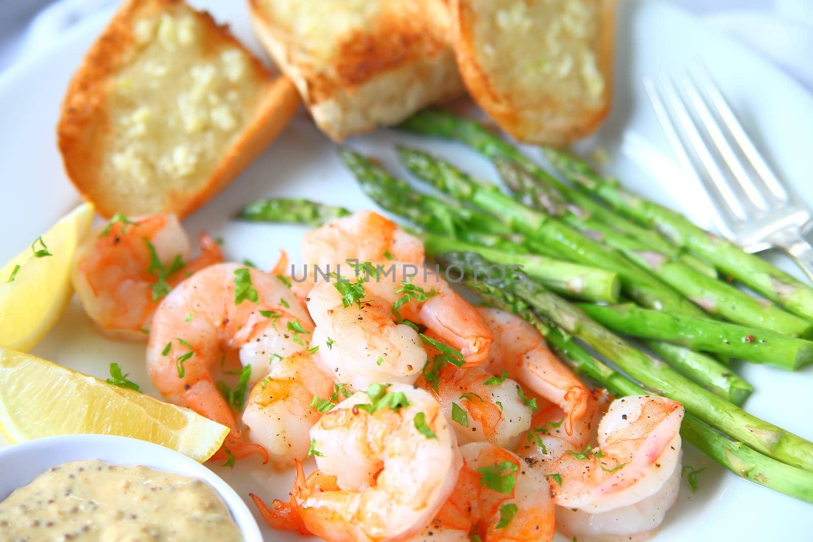 Plate of roasted shrimp and asparagus with garlic bread, lemon and mustard sauce