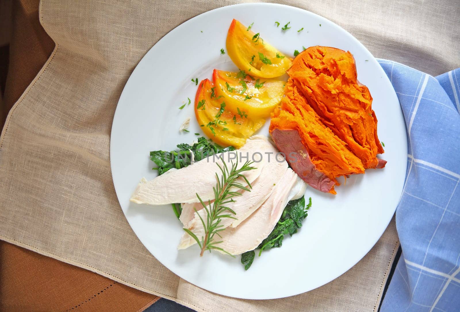 Overhead view of chicken dinner with baked yam, sauteed kale and heirloom tomato with napkins