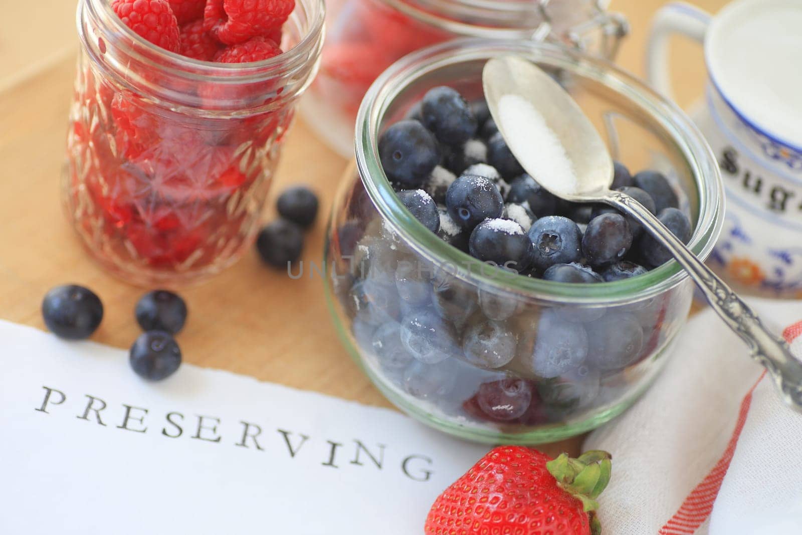 Blueberries, raspberries and strawberries in glass jars with sugar ready for making jam