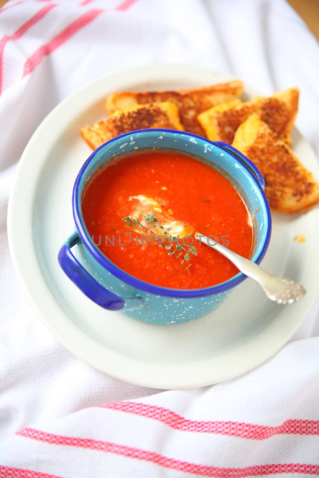 Overhead view of tomato soup with fresh thyme and a melted cheese sandwich cut into triangles