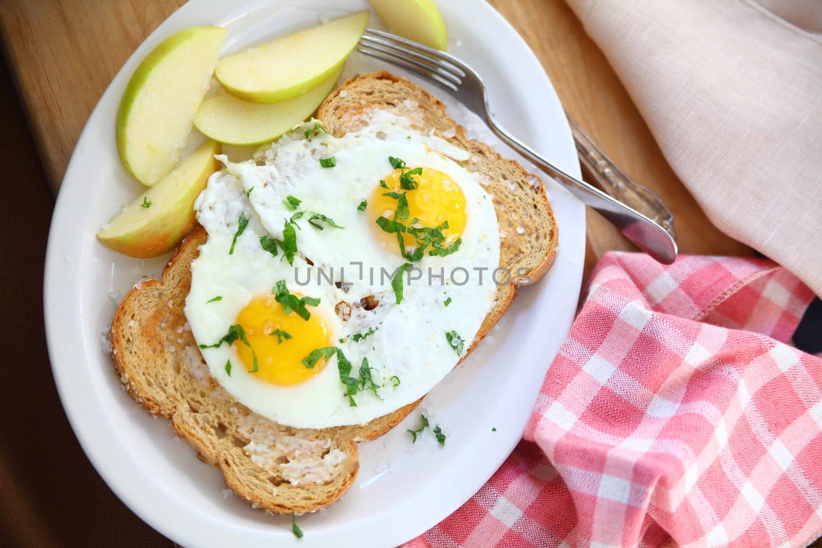 Overhead view of fried eggs on toast with coarse salt and apple slices