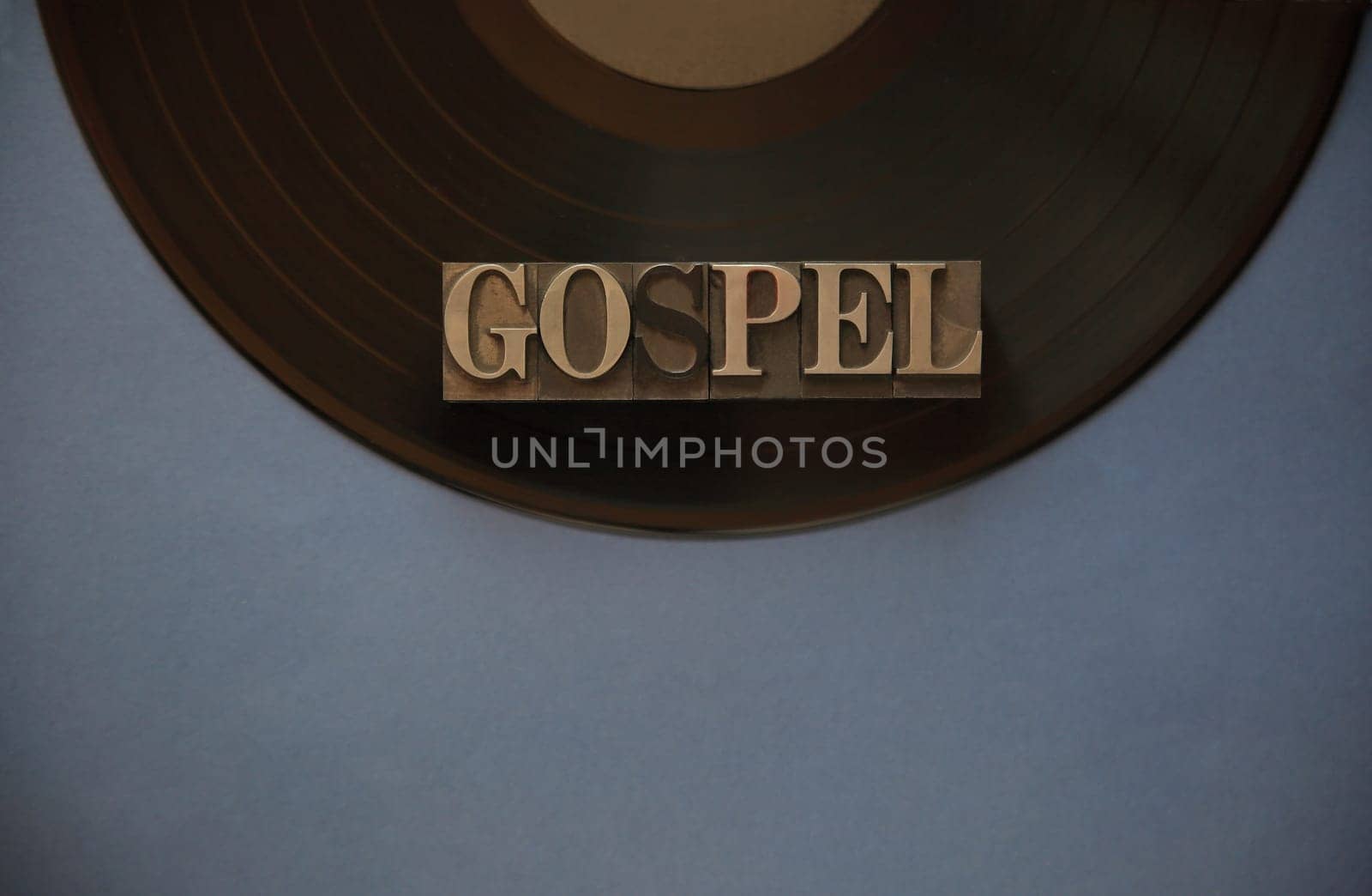 The word gospel in old metal type on a black vinyl record with a blue-gray background for text