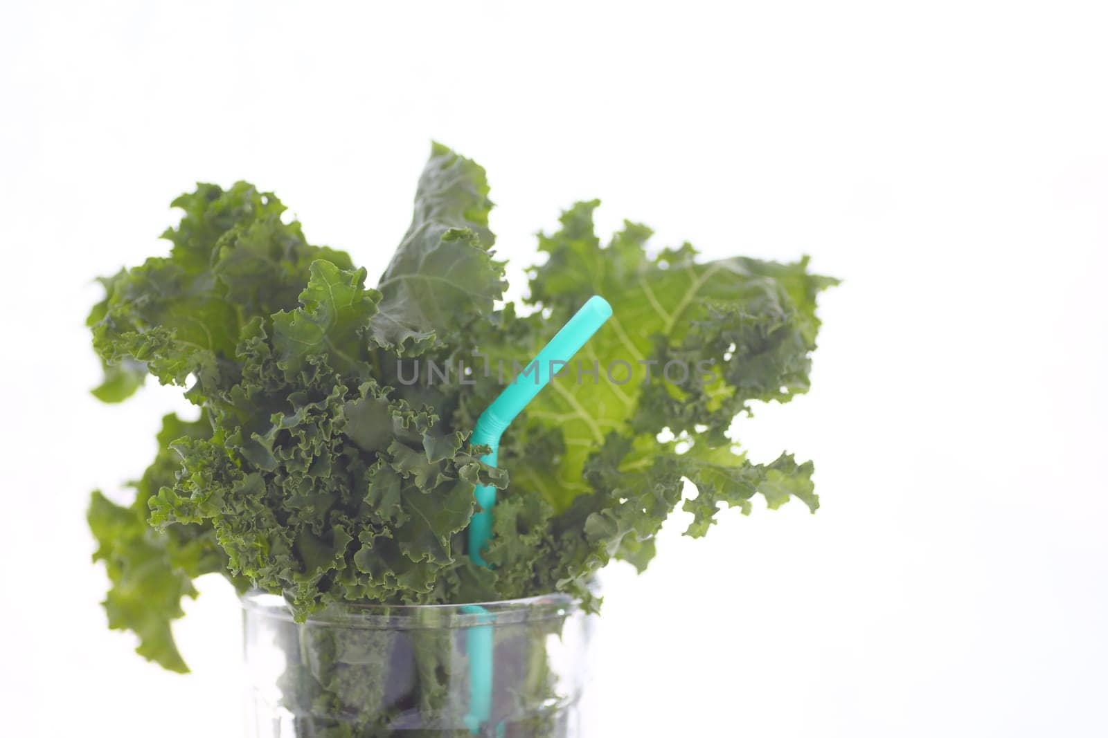 Fresh kale leaves in a drinking glass with a pale blue straw and copy space