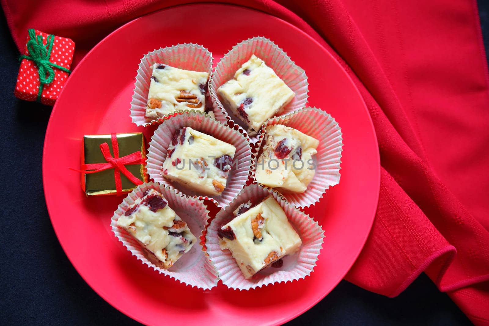 Plate of Christmas fudge made with white chocolate, cranberries and pecans with red napkin and miniature gifts