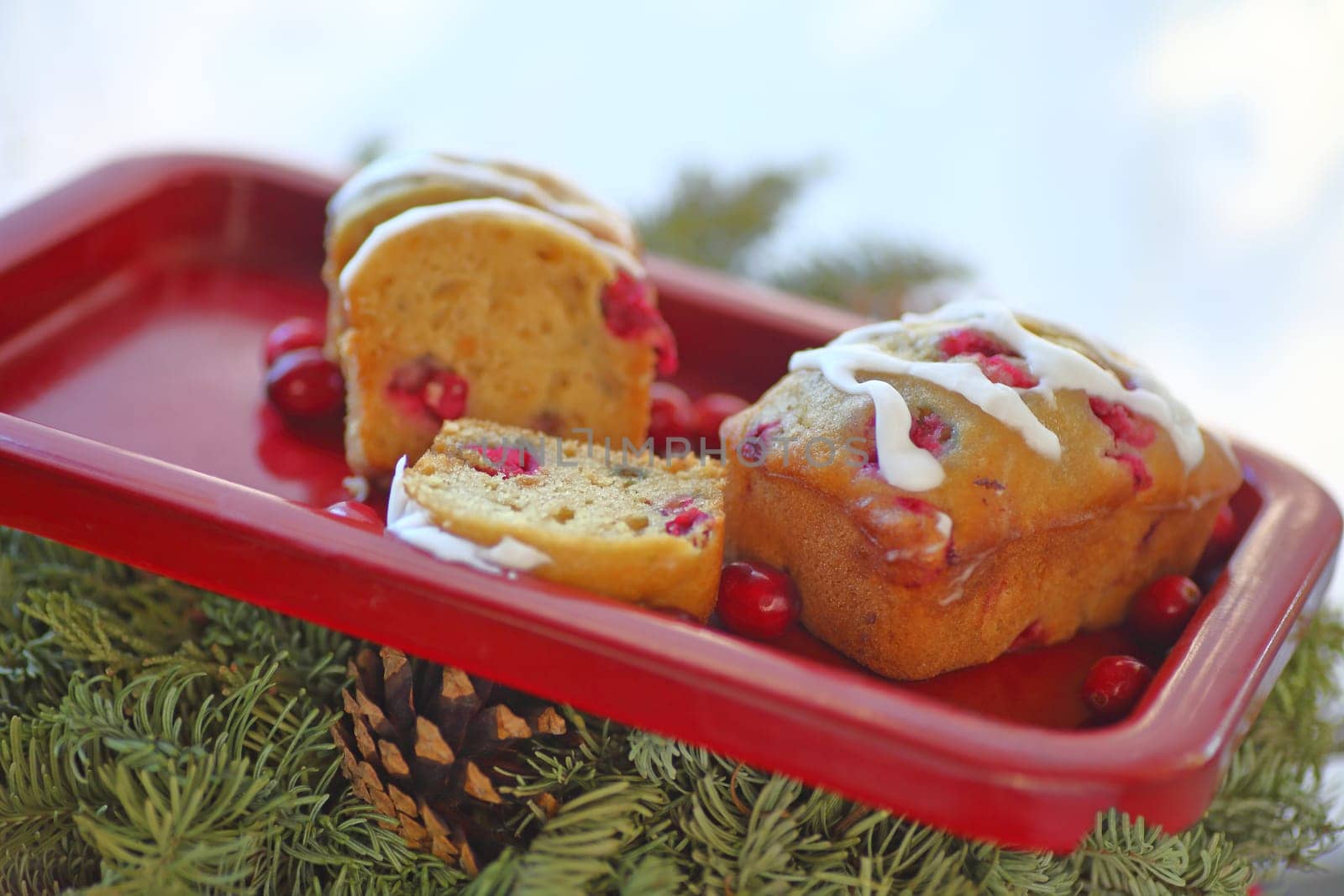 Small loaf cakes with fresh cranberries on a red tray over evergreens and a pine cone