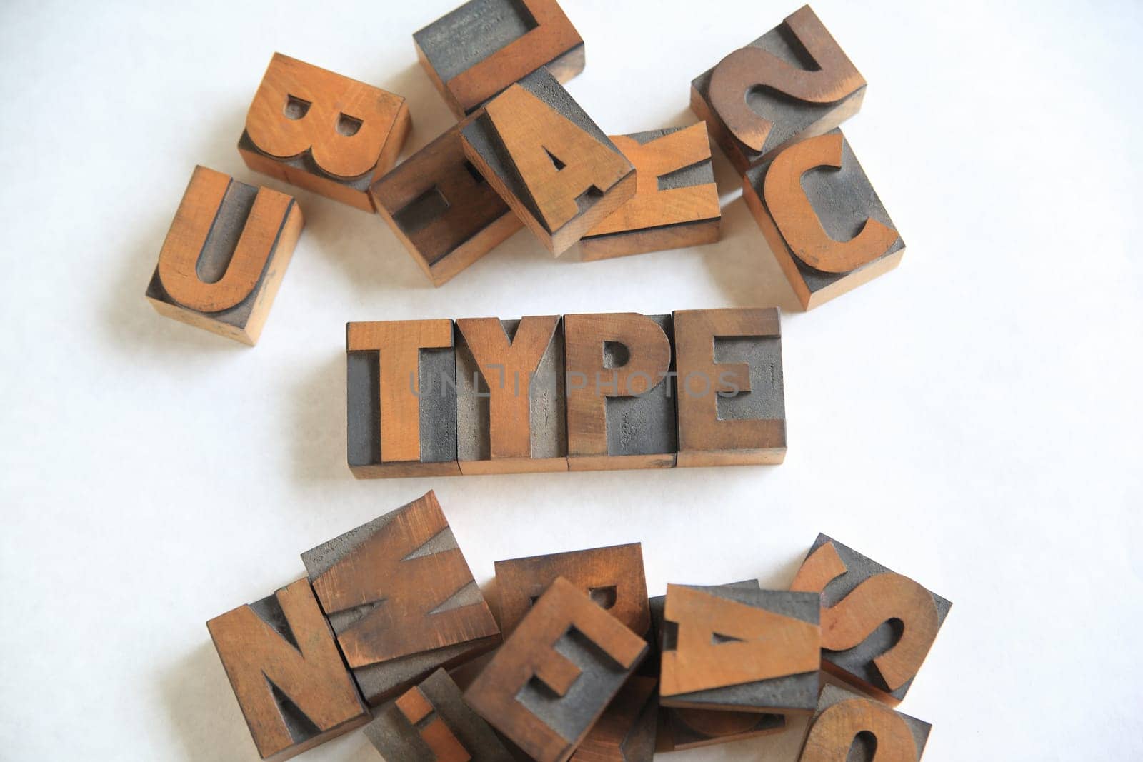Old letterpress wood letters form the word type on white with other alphabet letters alongside