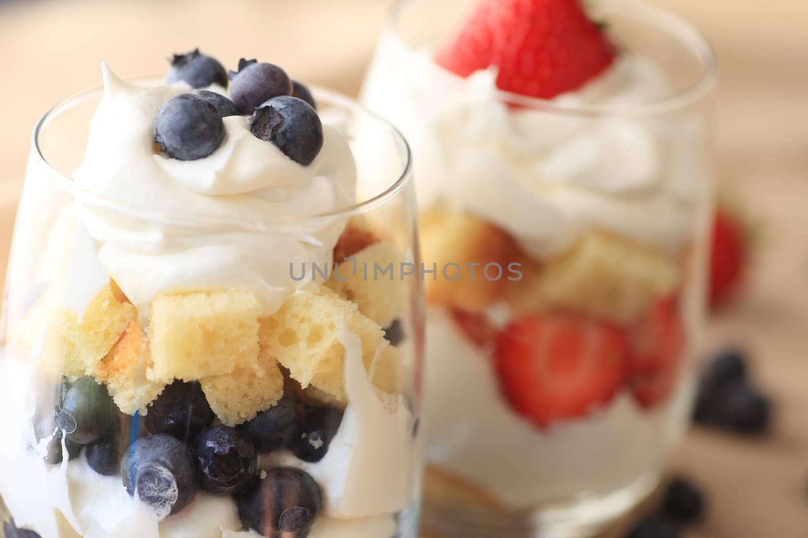 Glasses with fresh blueberry and strawberry trifles with cake and whipped cream