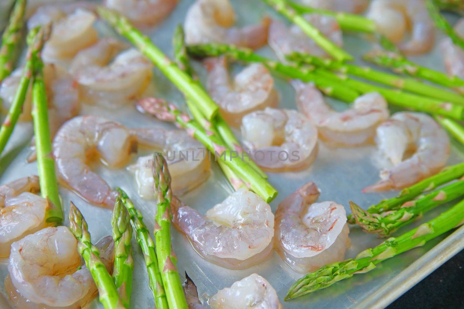 A baking sheet with raw shrimp, asparagus and olive oil