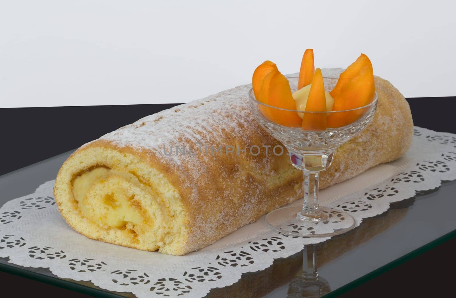 A sponge roll with apricot cream and fruits in a glass.