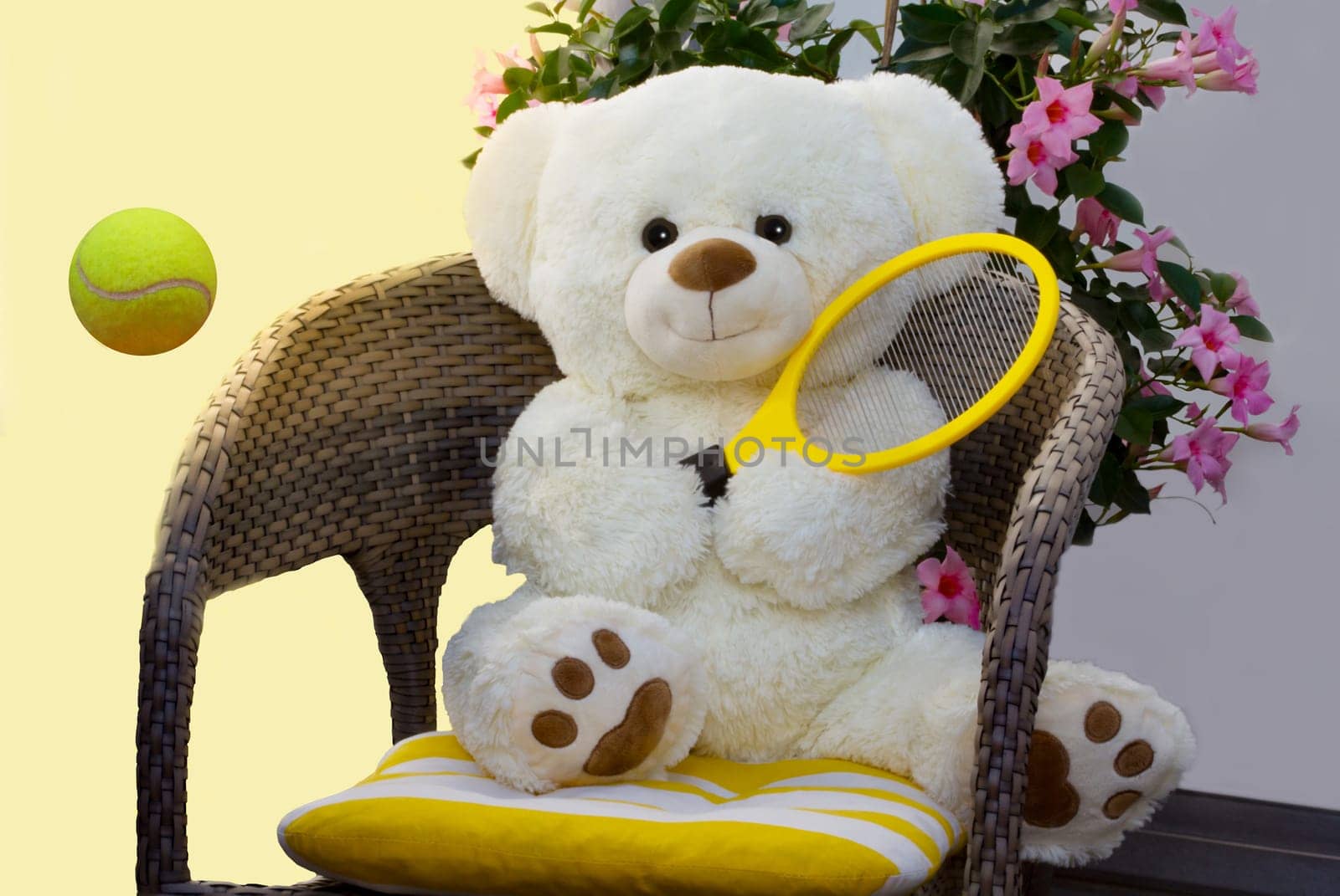 The teddy sits comfortably on the chair and plays tennis.