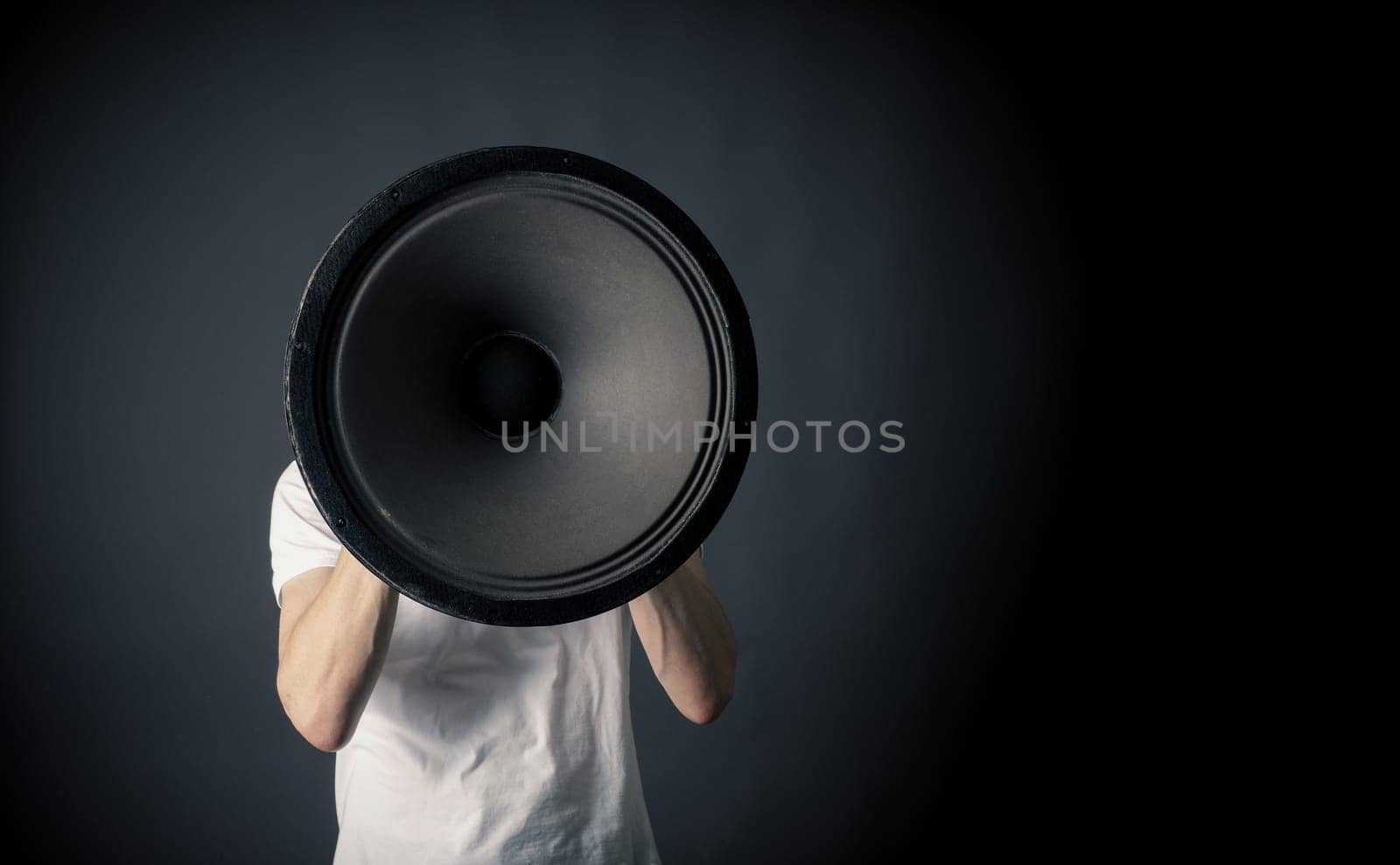 Young man holding a big speaker, speaking loud concept on a dark studio background with space for text or image
