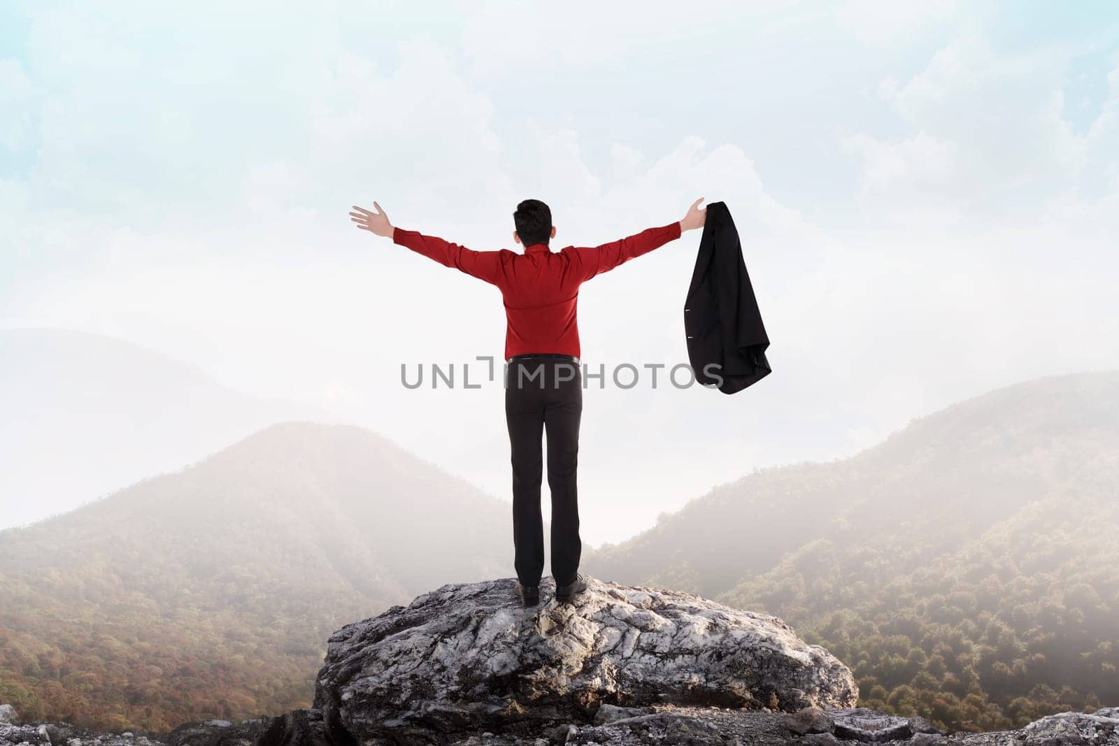Asian business man standing on the top of mountain, raise hand and open his suit