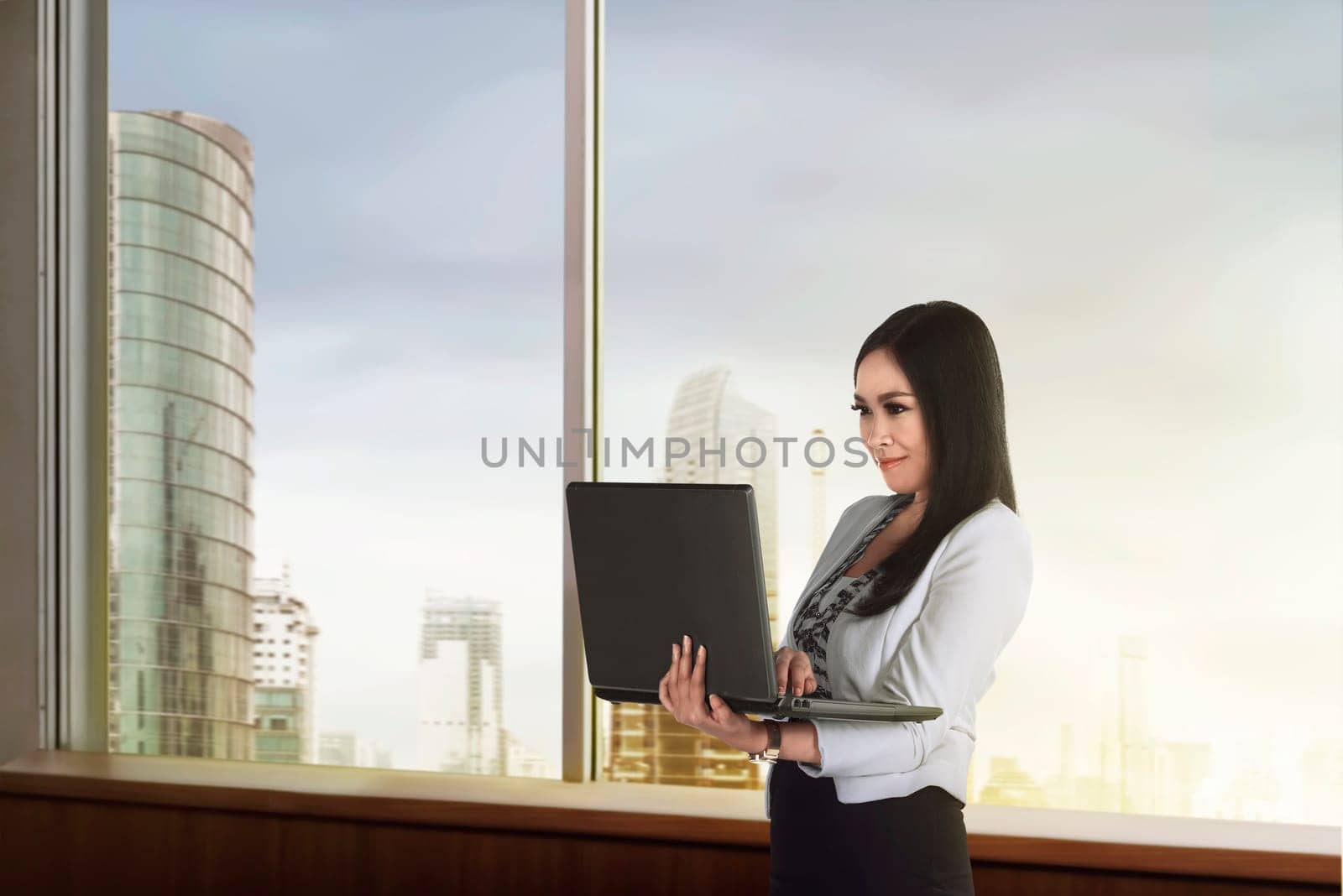 Beautiful asian businesswoman holding laptop in her office on a building background