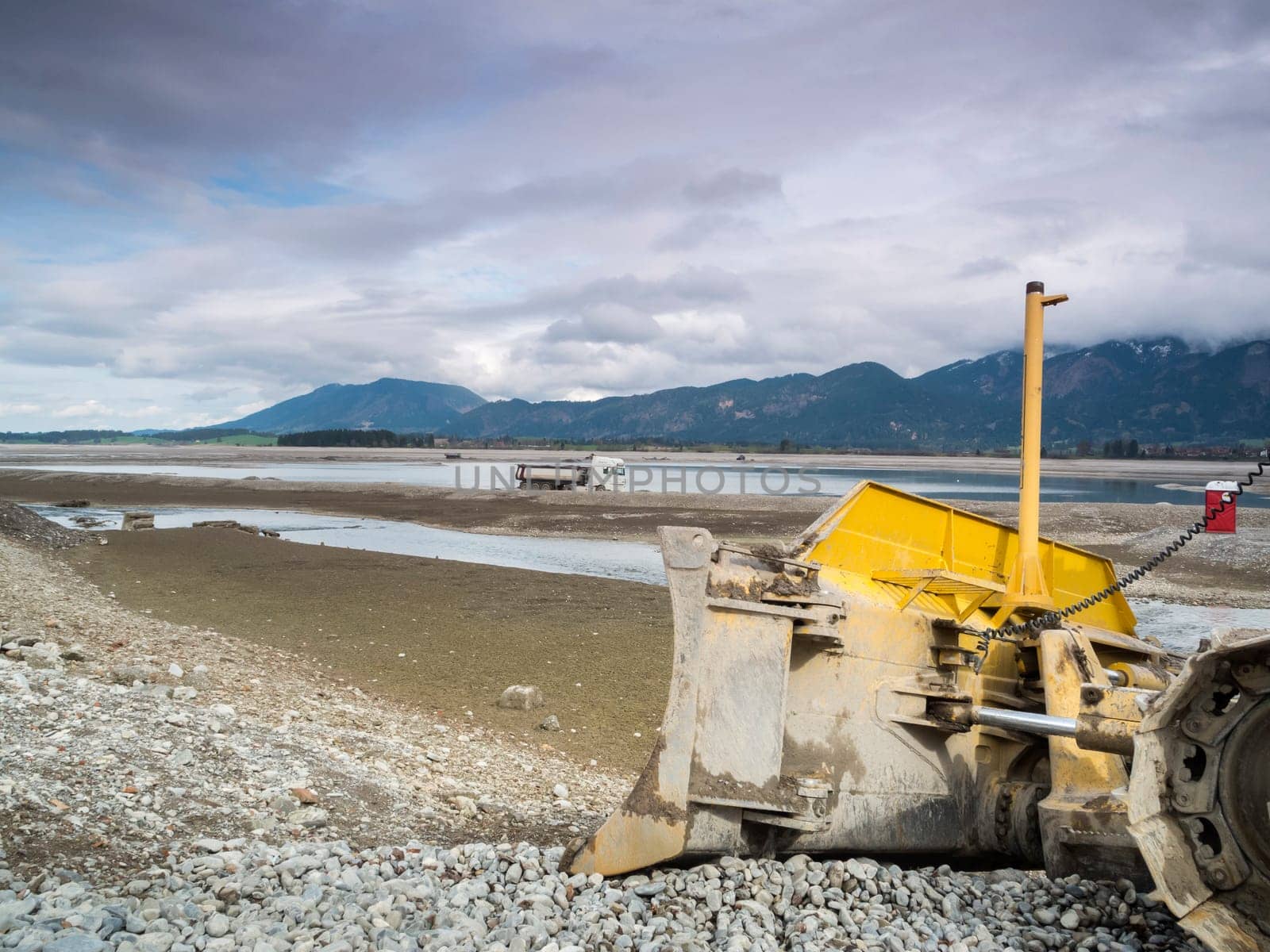 Bulldozer in the drained Forggensee near Füssen / Bavaria. The Forggensee is fed by thawing snow from the high Alps and is a reservoir for sedimentary rocks. In spring,the lake is emptied to remove the sedimentary rock. In summer,the lake has returned to its normal water level and is navigated by excursion boats.