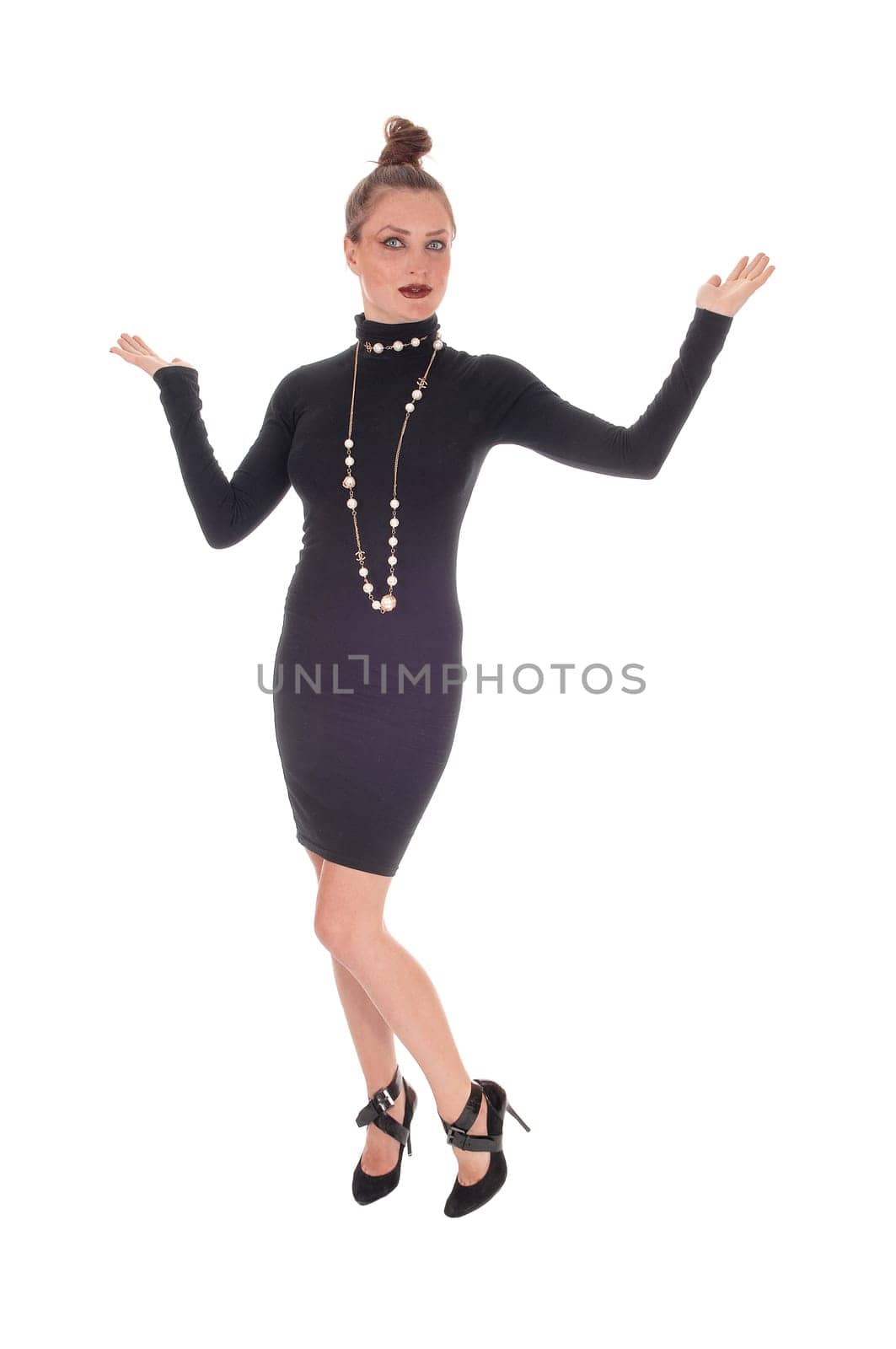 A beautiful young Caucasian woman in a black dress and necklace.dancing with her arms up, isolated for white background..