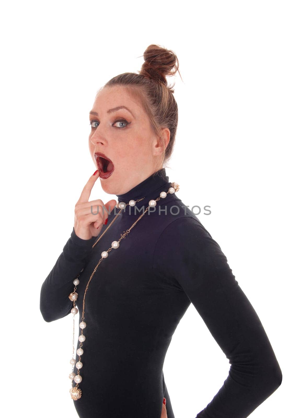 A beautiful young woman standing in profile waist up with her finger.on her open mouth, amazed, isolated for white background..