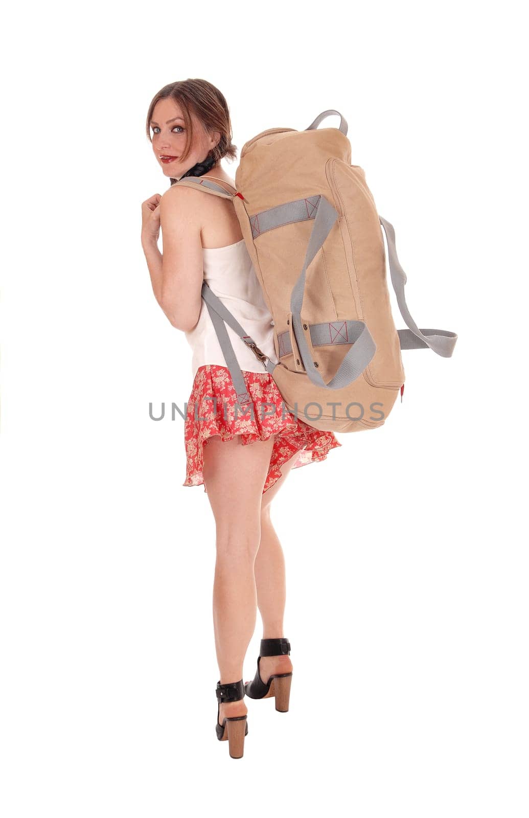 A beautiful young woman in shorts and heels caring an big heavy.backpack, ready for a hike, isolated for white background..