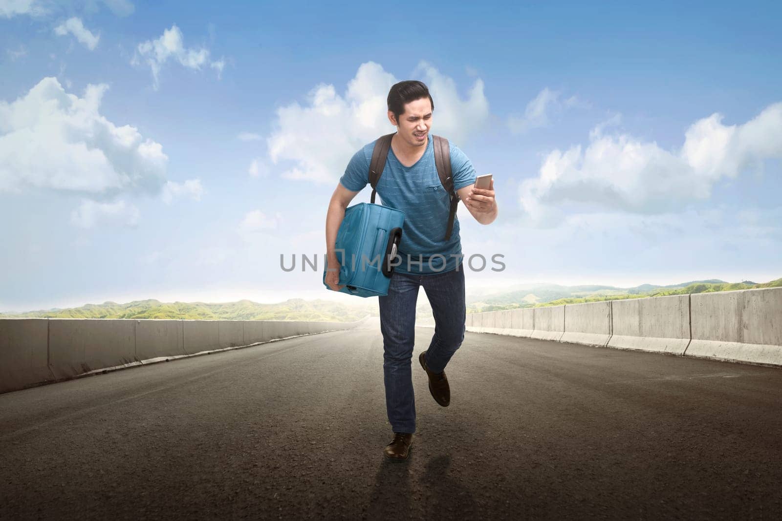 Young asian tourist running with holding phone and suitcase on the road