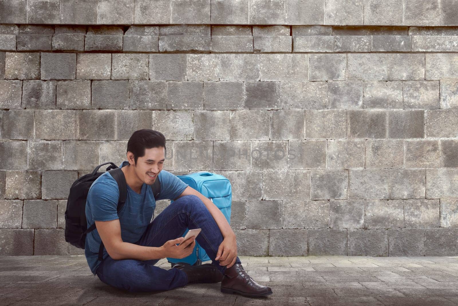 Handsome asian backpacker with phone resting against ancient wall background