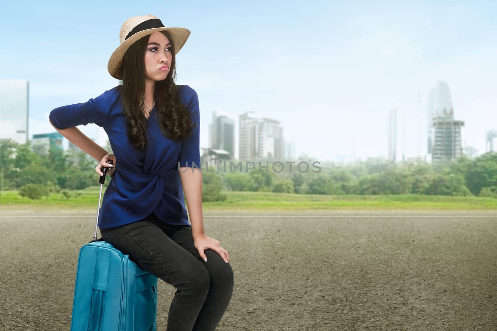 Traveler asian woman with hat sitting on a suitcase on the urban road