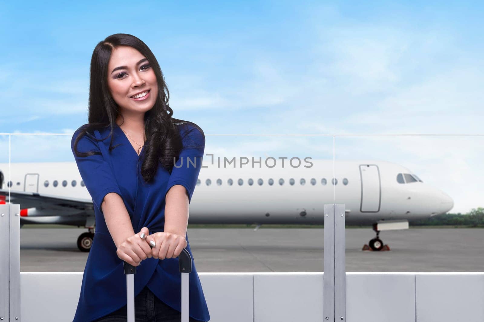 Young asian woman holding suitcase in the airport with airplane on background