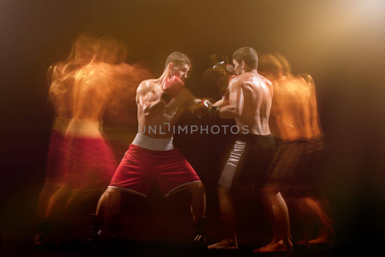 The two male athlete boxers punching with dramatic edgy lighting in a dark studio. Image made with stroboscope