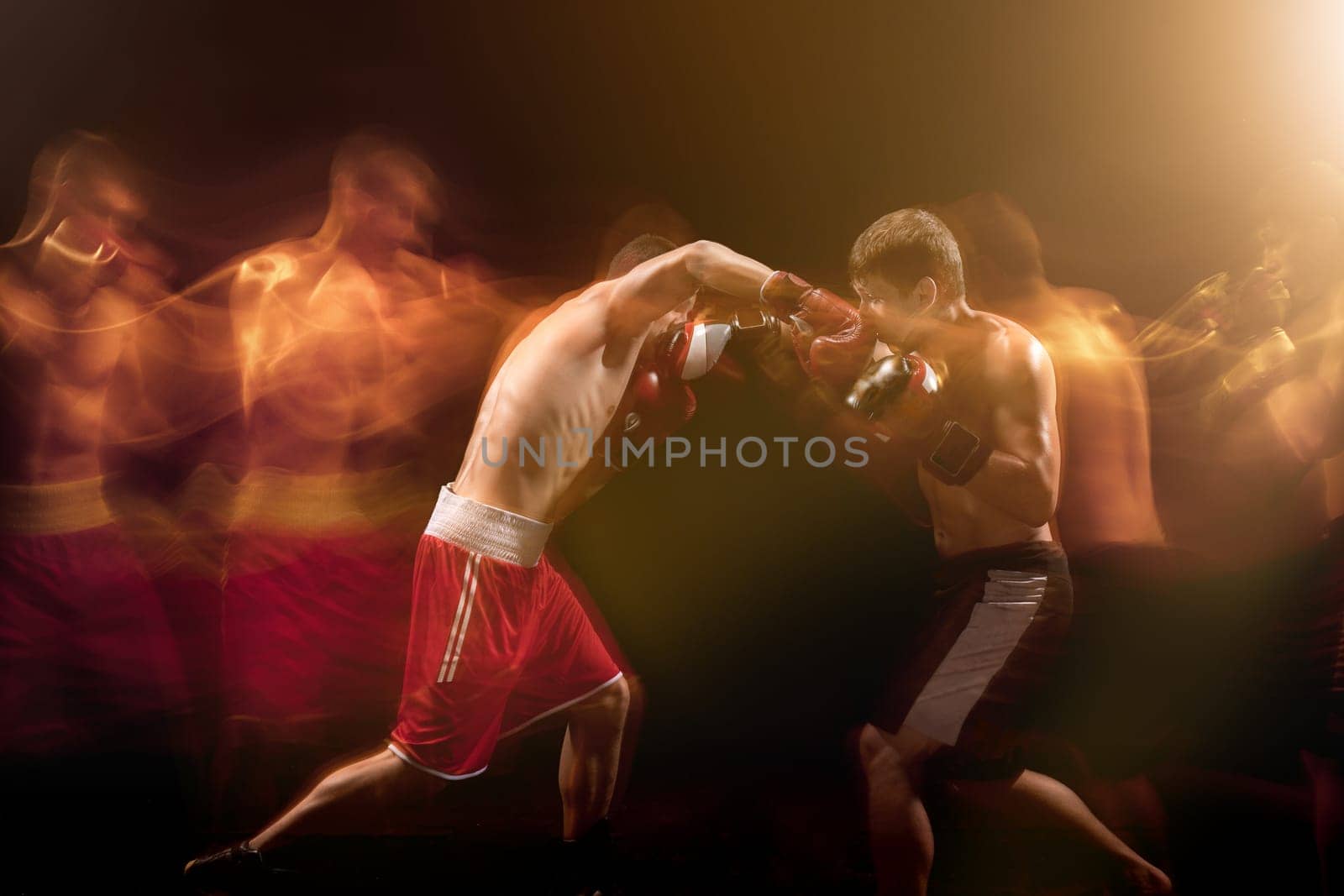 The two male athlete boxers punching with dramatic edgy lighting in a dark studio. Image made with stroboscope