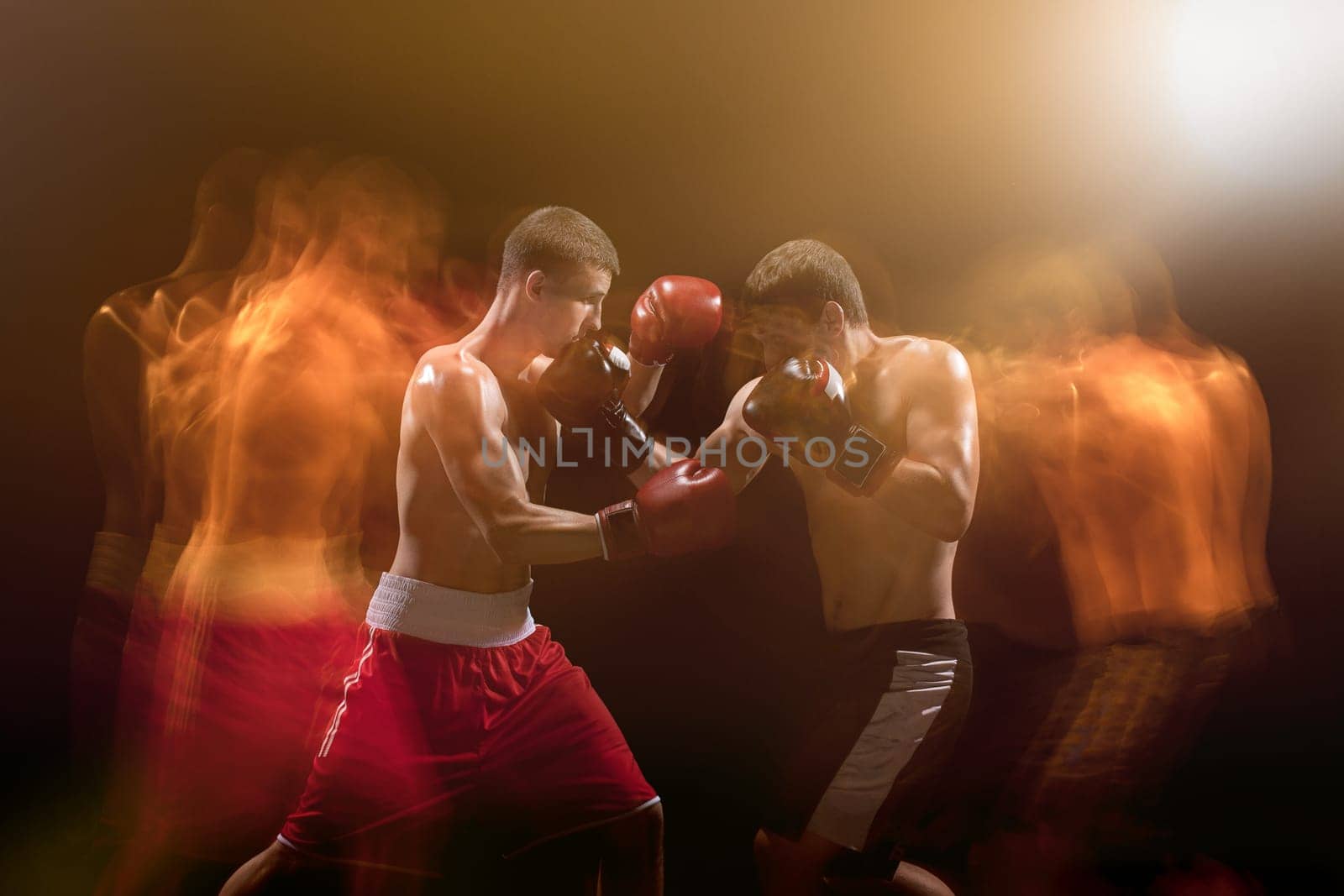 The two male athlete boxers punching with dramatic edgy lighting in a dark studio. Image made with stroboscope