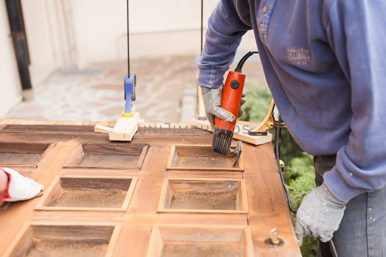 Carpenter at work with angular Sander. Maintenance and restoration of an old wooden door.