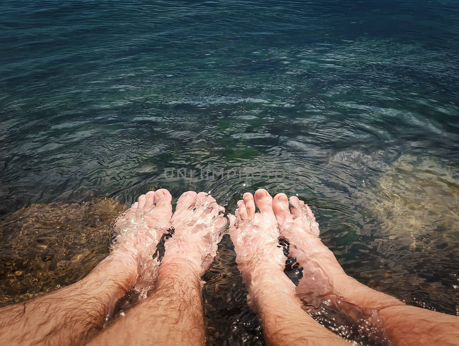 Close up of two male legs in the clear sea water. Summer vacation, resting and relaxation concept