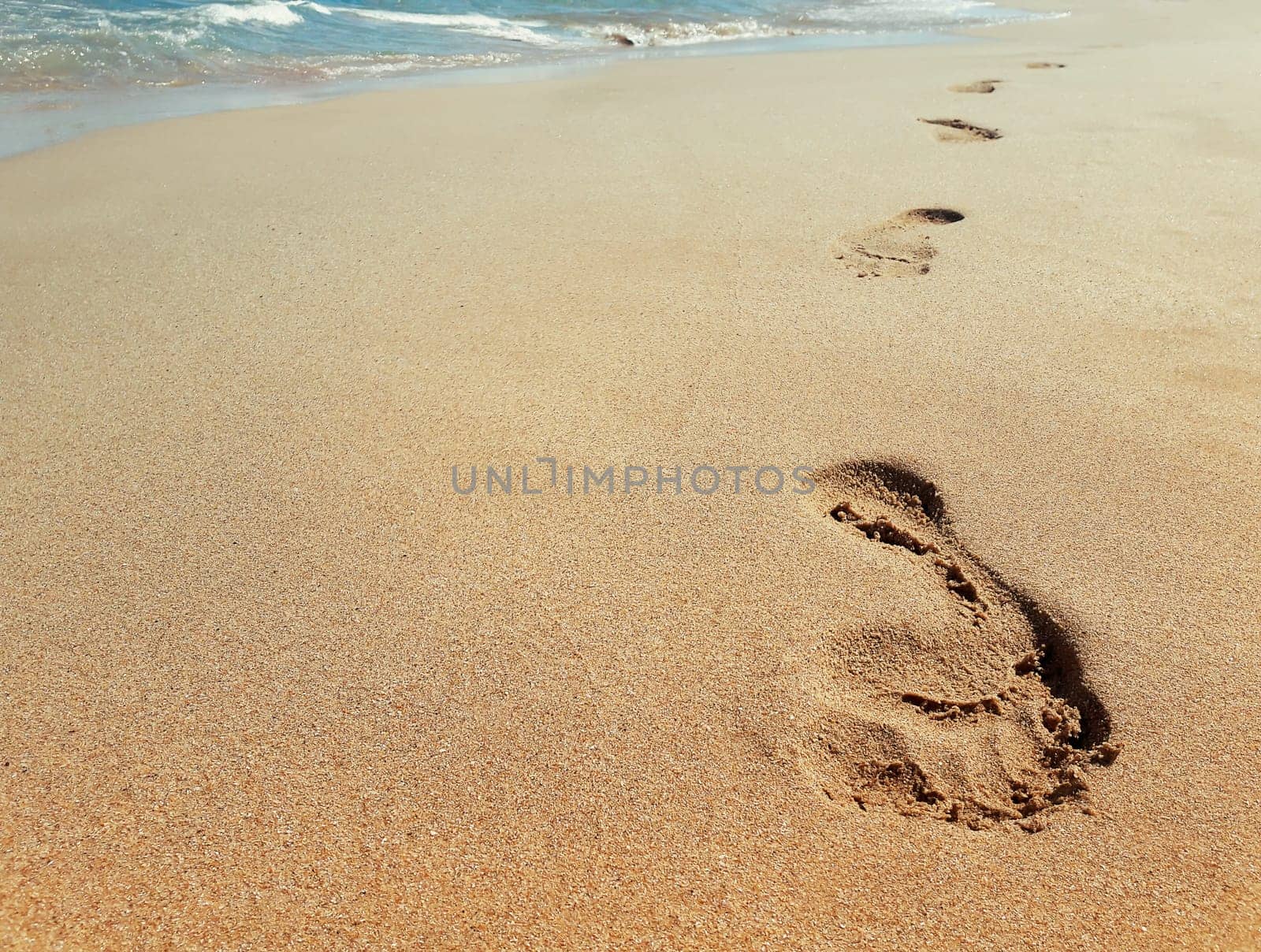 Closeup of footprints in sand at the beach near the water. Journey concept
