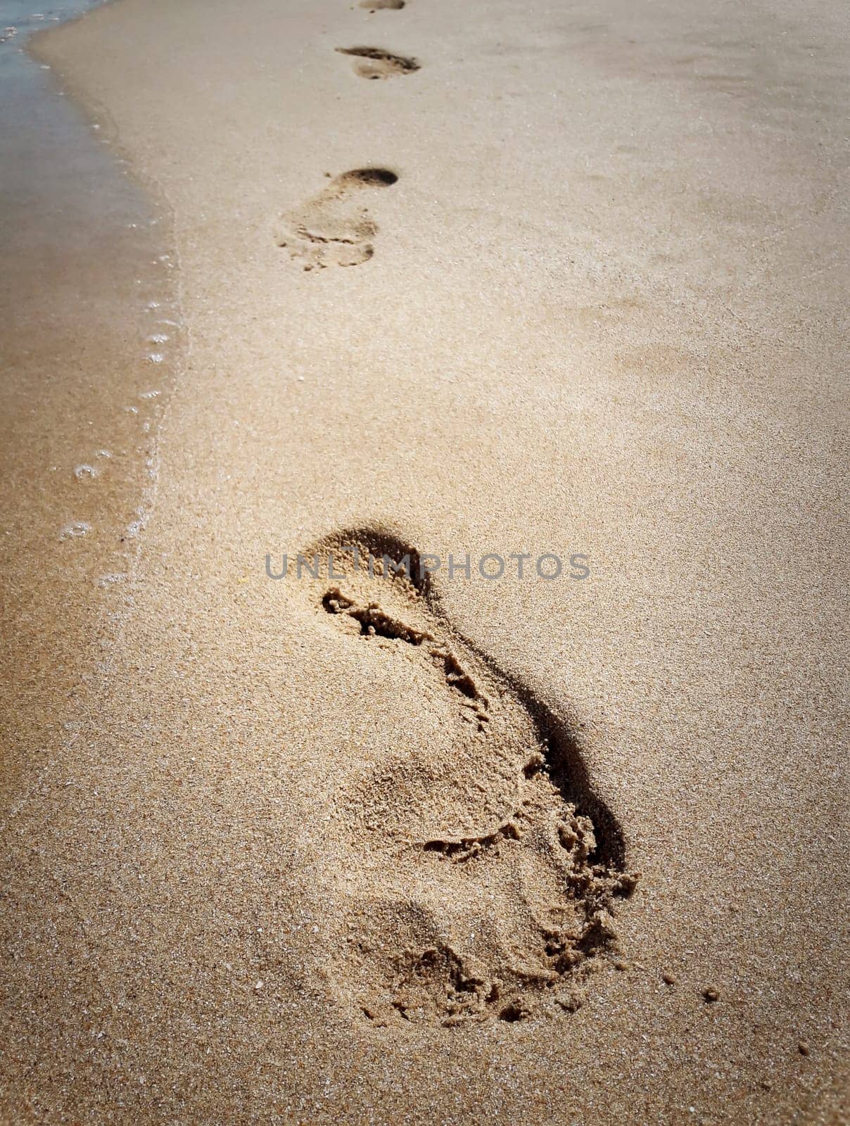 Closeup of footprints in sand at the beach near the water. Journey concept