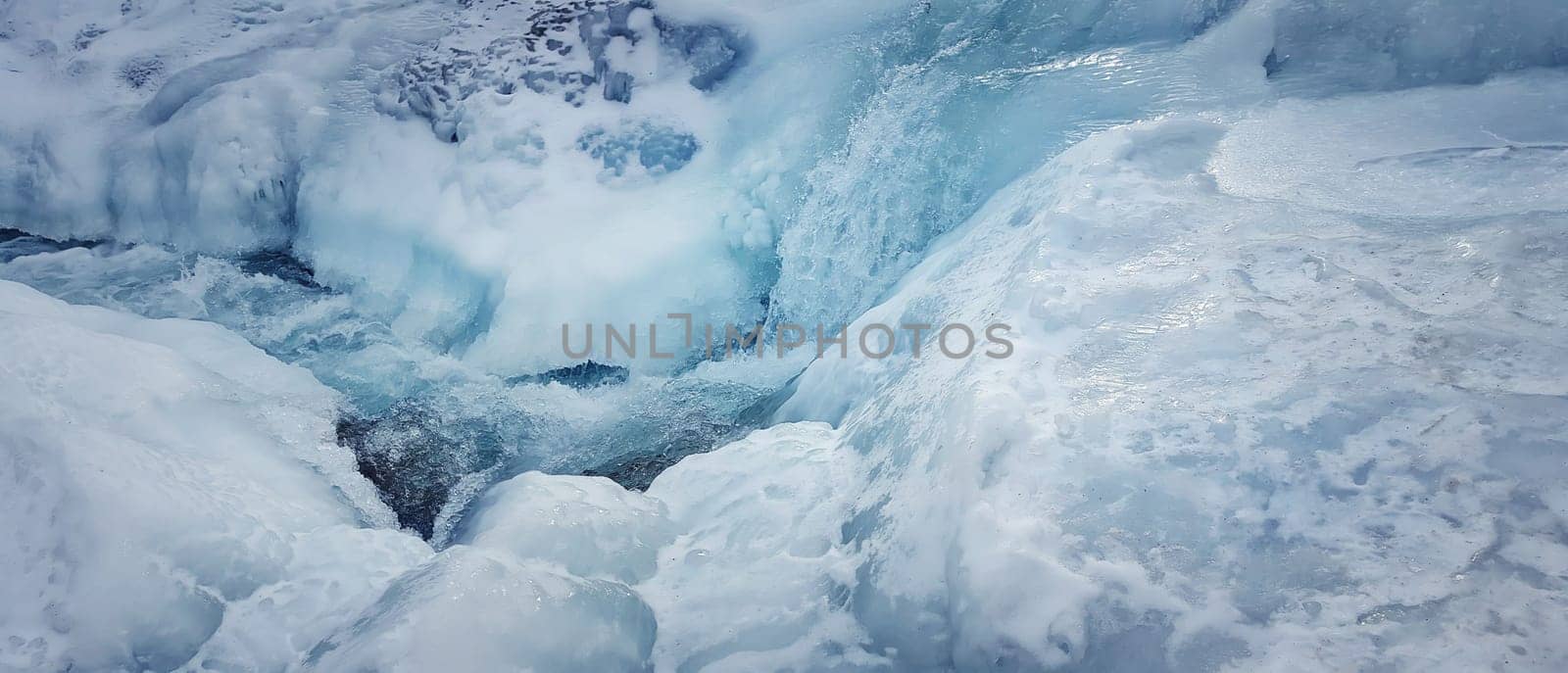 Abstract frozen river background, very cold winter, as blue water flows through the snowy ice.