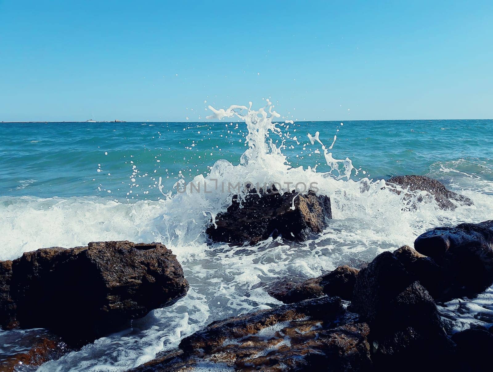 Big sea waves breaking on the stony beach forming foam and splash