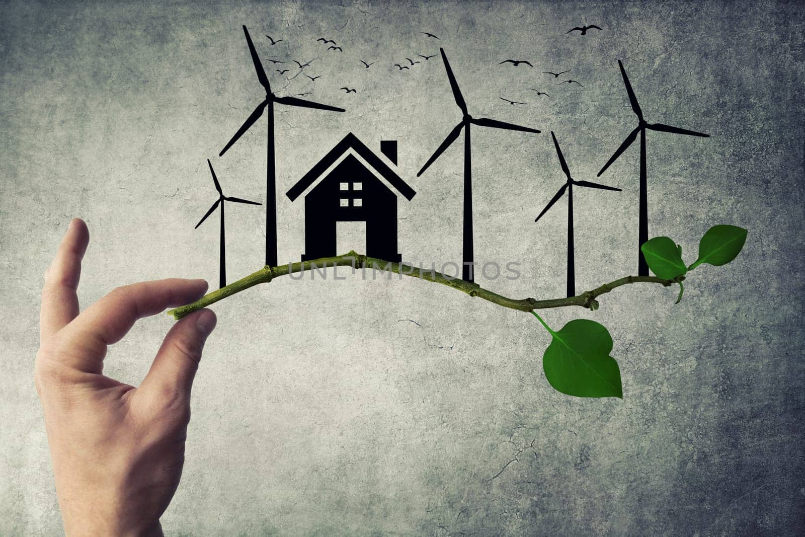 Human hand holding a tree branch. Environmental green energy concept. Silhouette of house, wind turbine and birds flying