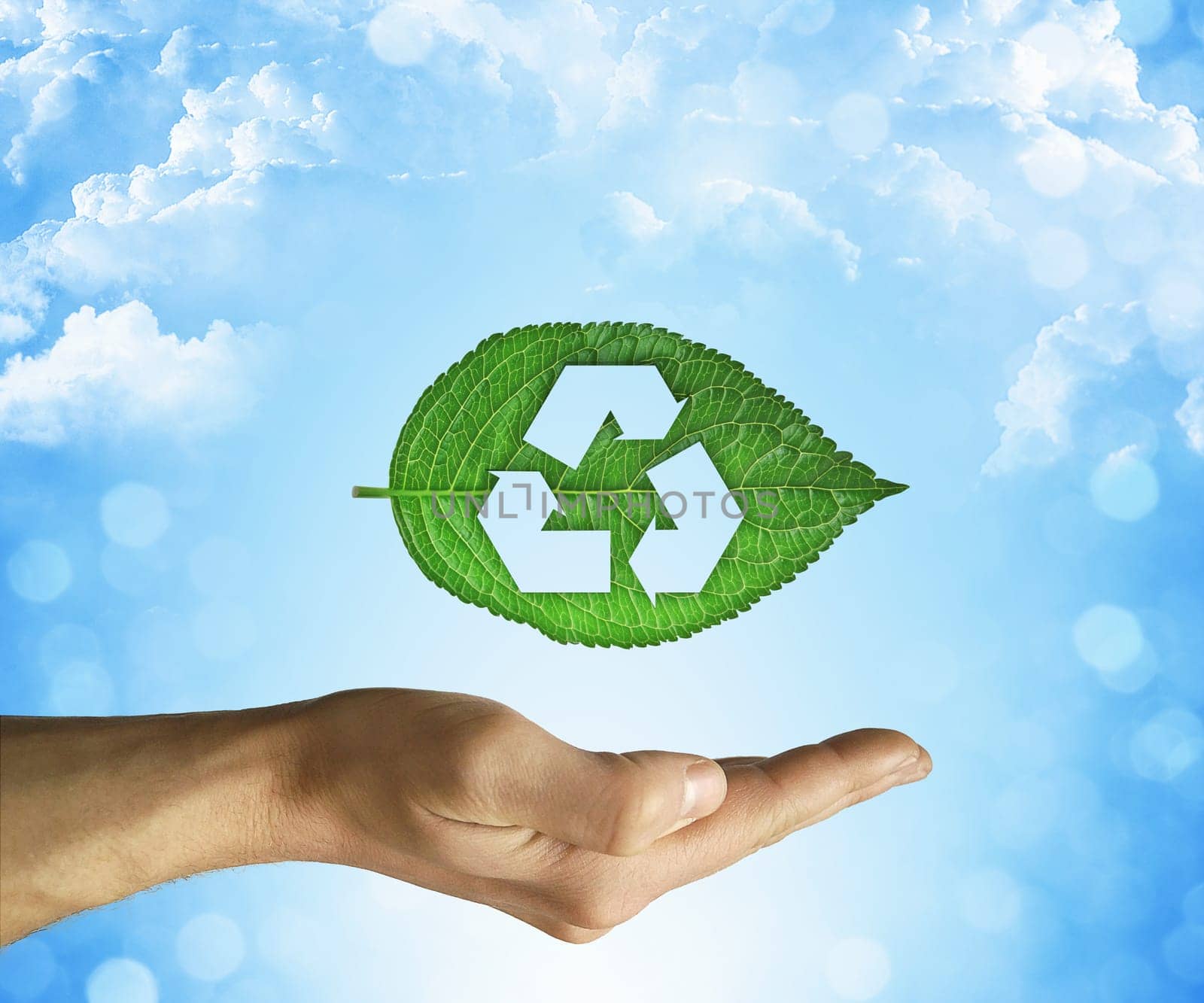 Opened hand holding a green leaf with recycling symbol on a blue sky background. Friendly environment and sustainable development concept