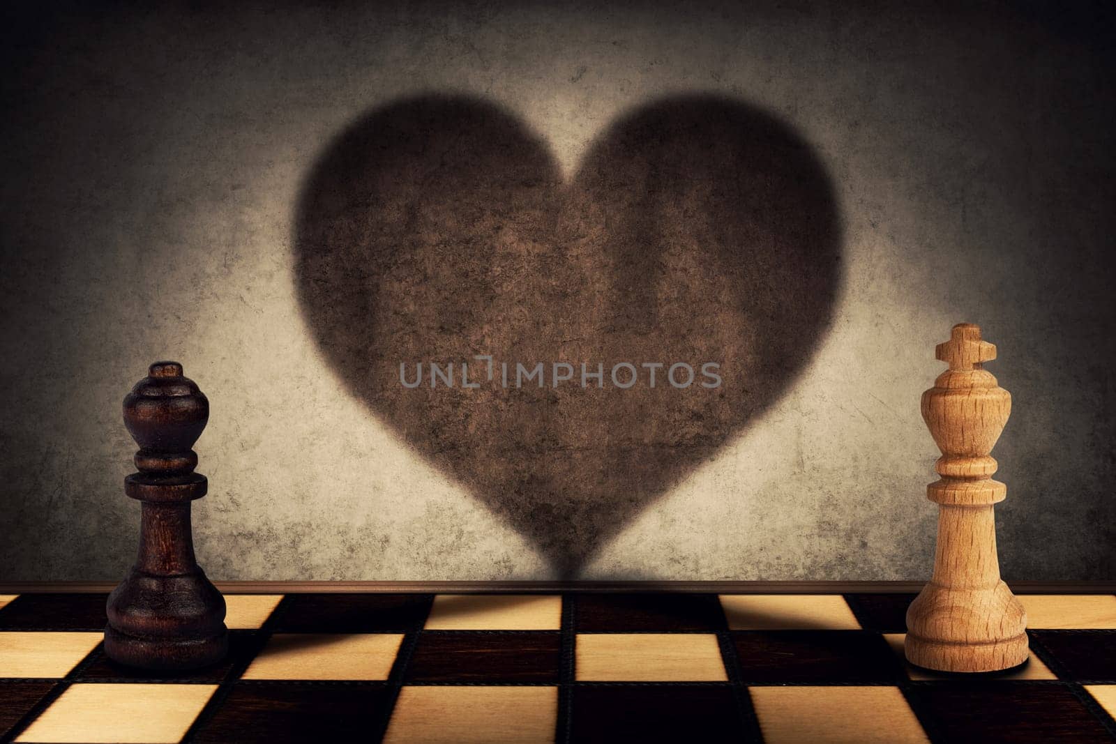 Black queen and white king chess pieces standing in front one another casting their shadows transform into a big heart on the wall. Love symbol, impossible relationship, togetherness concept.