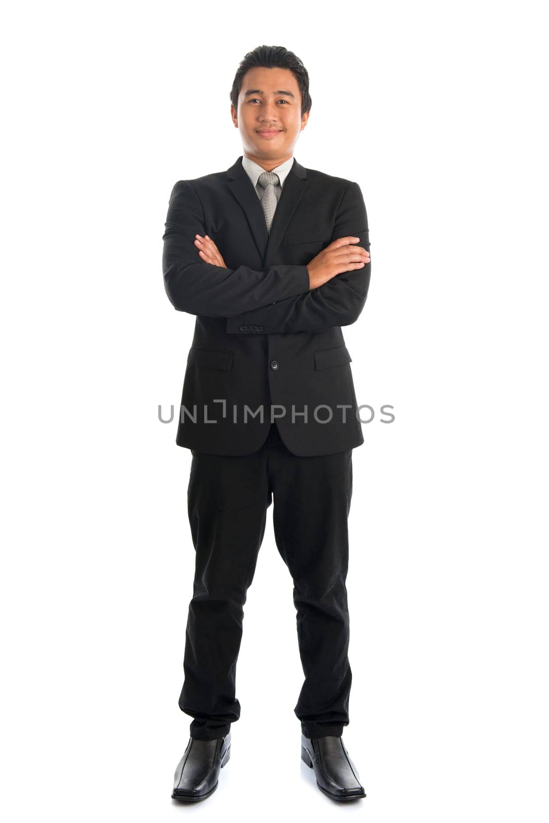 Full body front view of arm crossed young Southeast Asian businessman standing isolated on white background.