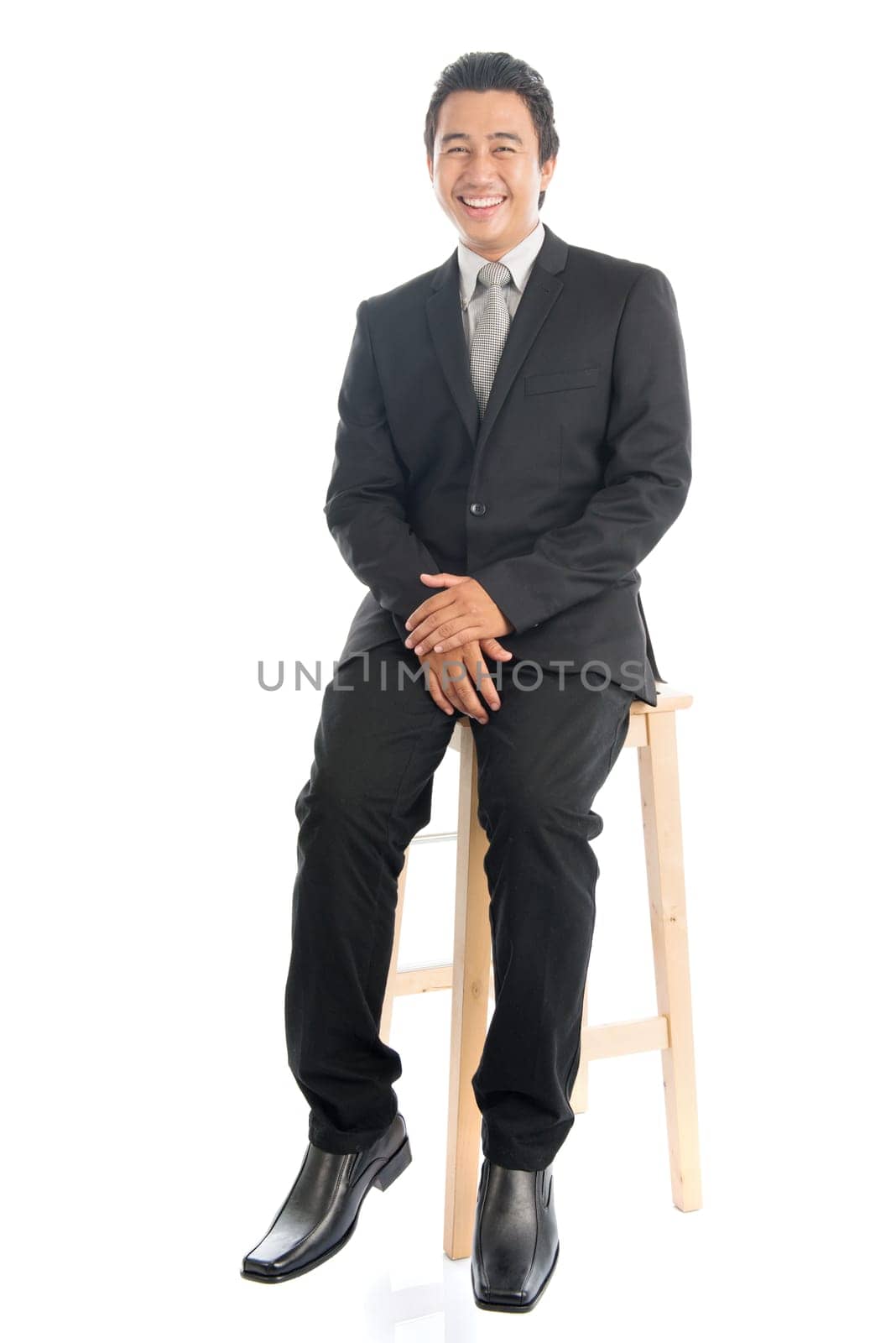 Full body portrait of happy young Southeast Asian businessman sitting on high chair, isolated on white background.