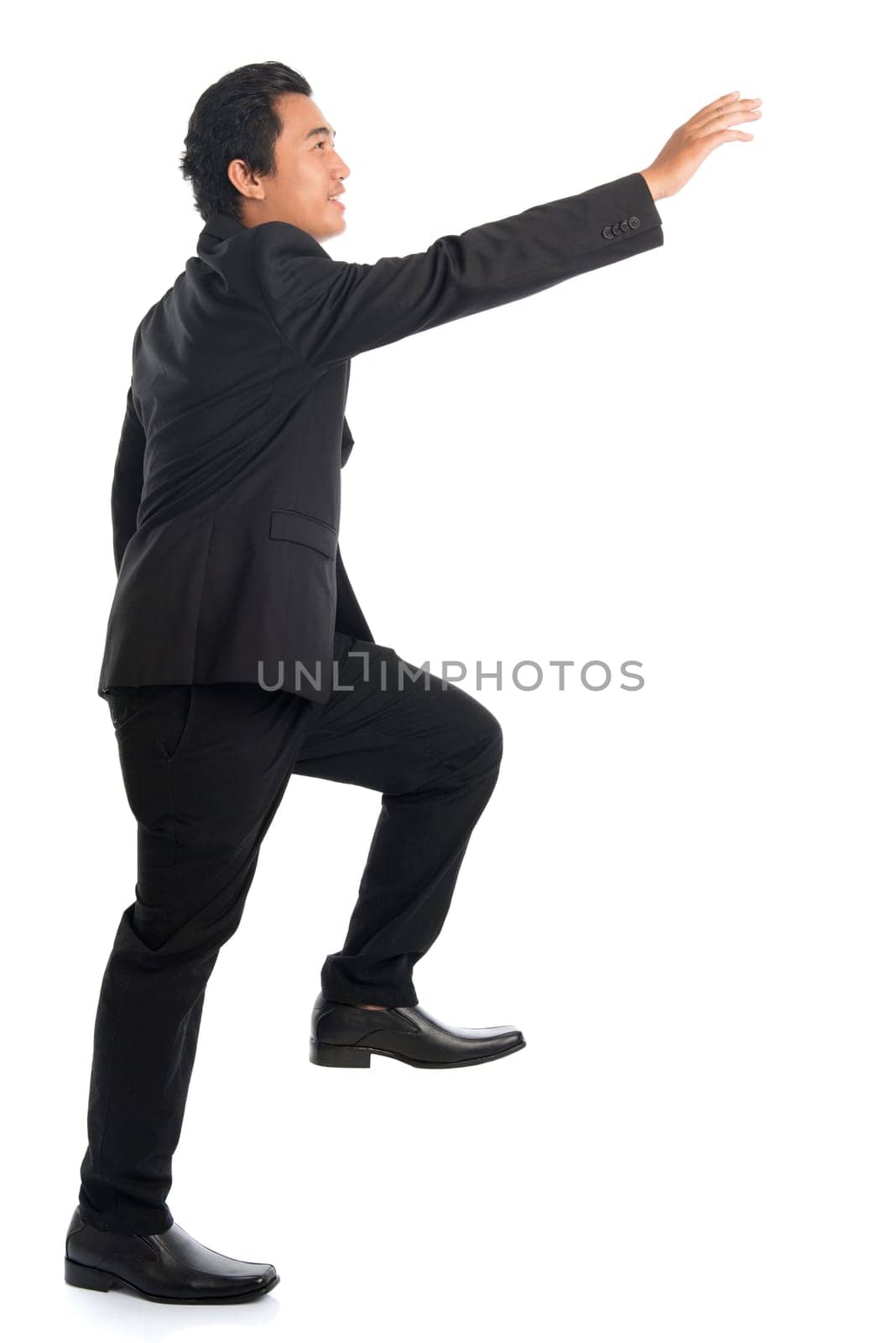 Full body side view of attractive young Southeast Asian businessman stepping up stair case and hand reaching something, isolated on white background.