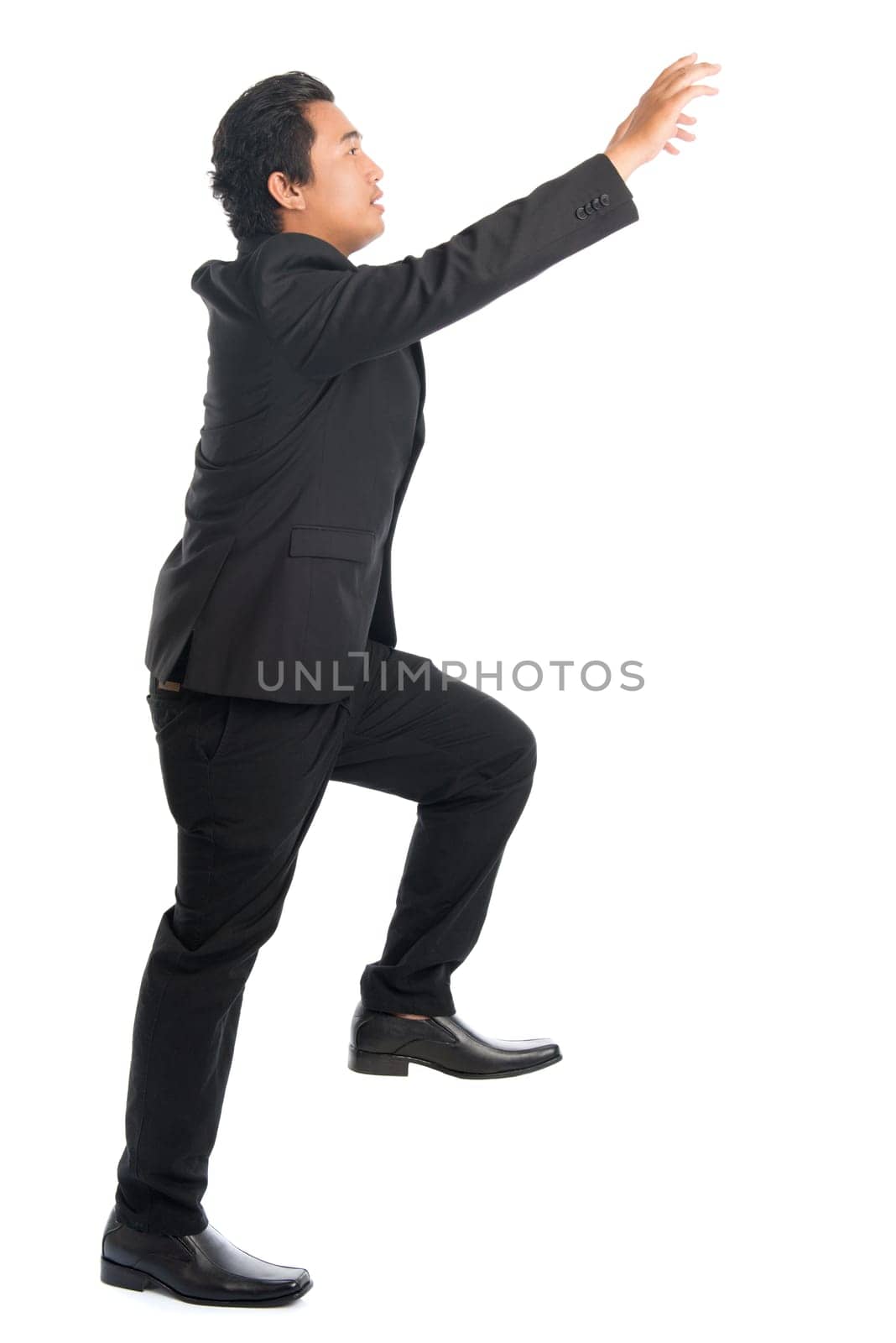 Full body side view of young Southeast Asian businessman stepping up stair case and hand grabbing something, isolated on white background.