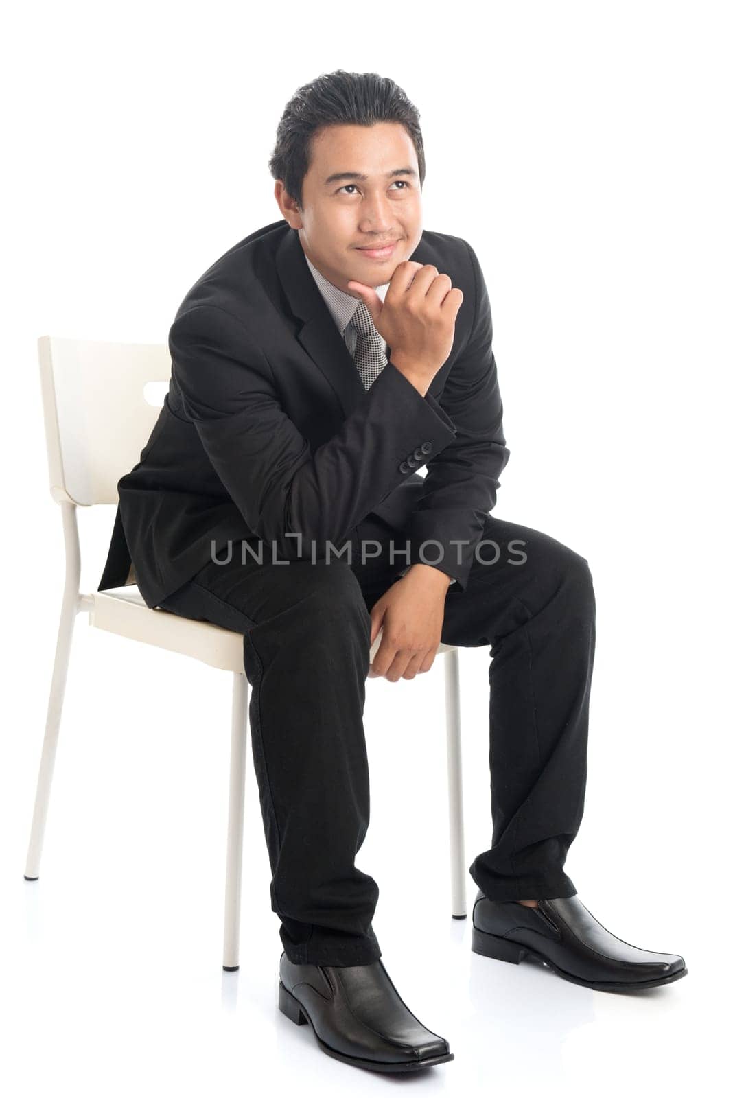 Full body portrait of attractive young Southeast Asian businessman sitting on a chair and thinking, isolated on white background.