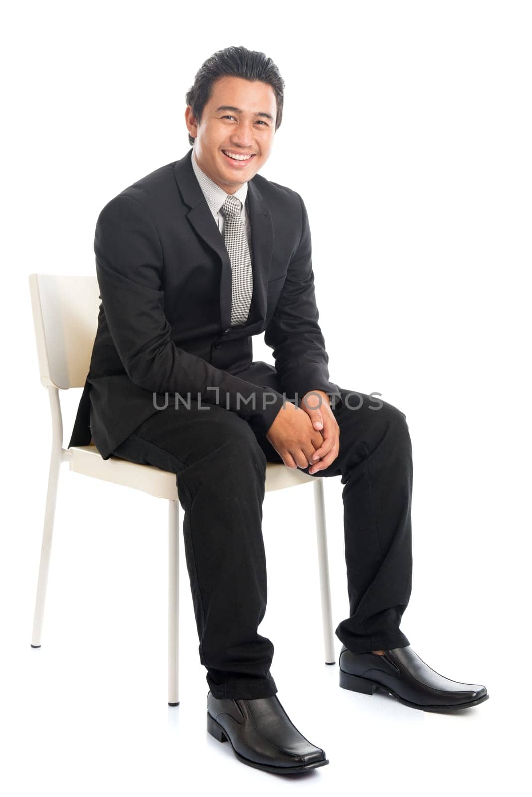 Full body portrait of attractive young Southeast Asian businessman sitting on a chair, isolated on white background.
