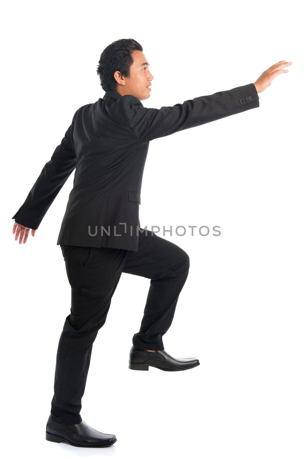 Full body side view of attractive young Southeast Asian businessman stepping up stair case and hand grabbing something, isolated on white background.