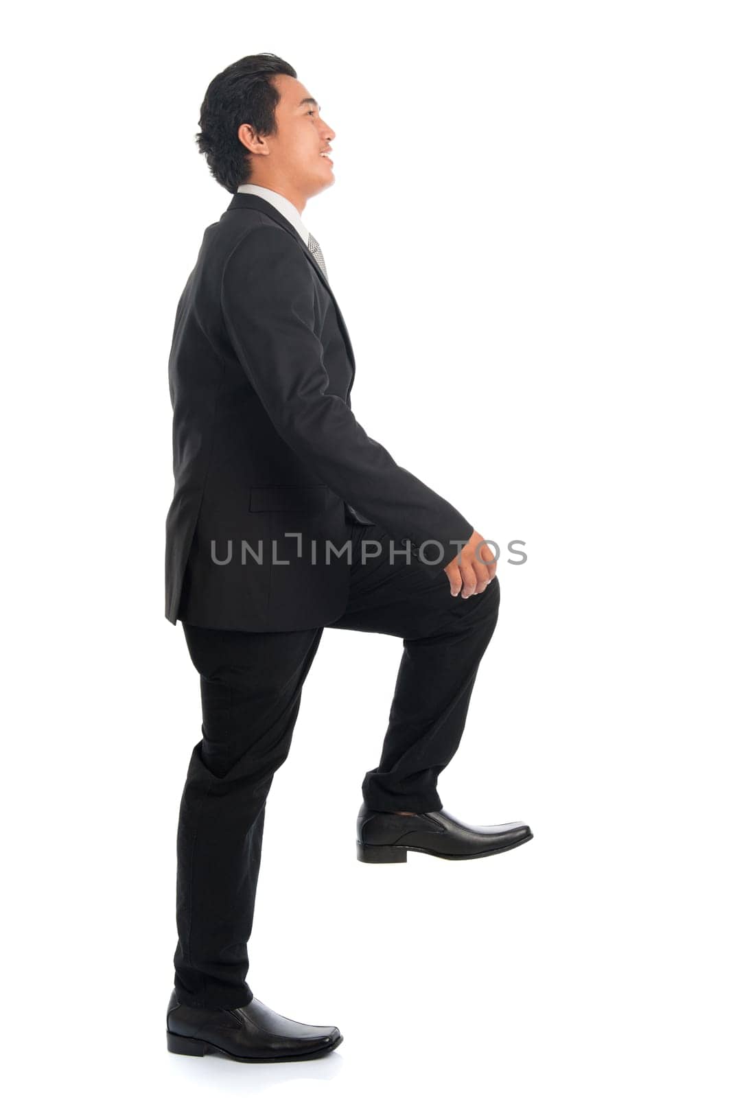 Full body side view of attractive young Southeast Asian businessman stepping up stair case, isolated on white background.